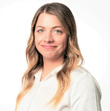 A woman with long, wavy blonde hair wearing a white shirt smiles at the camera against a plain white background.
