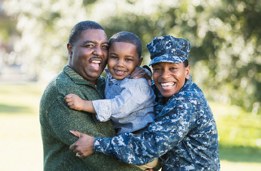 A smiling man, a woman in military uniform, and a young boy embrace outdoors in a sunny park, all appearing happy—a moment that captures the spirit of community fostered by the Clarvida MSEP partnership.